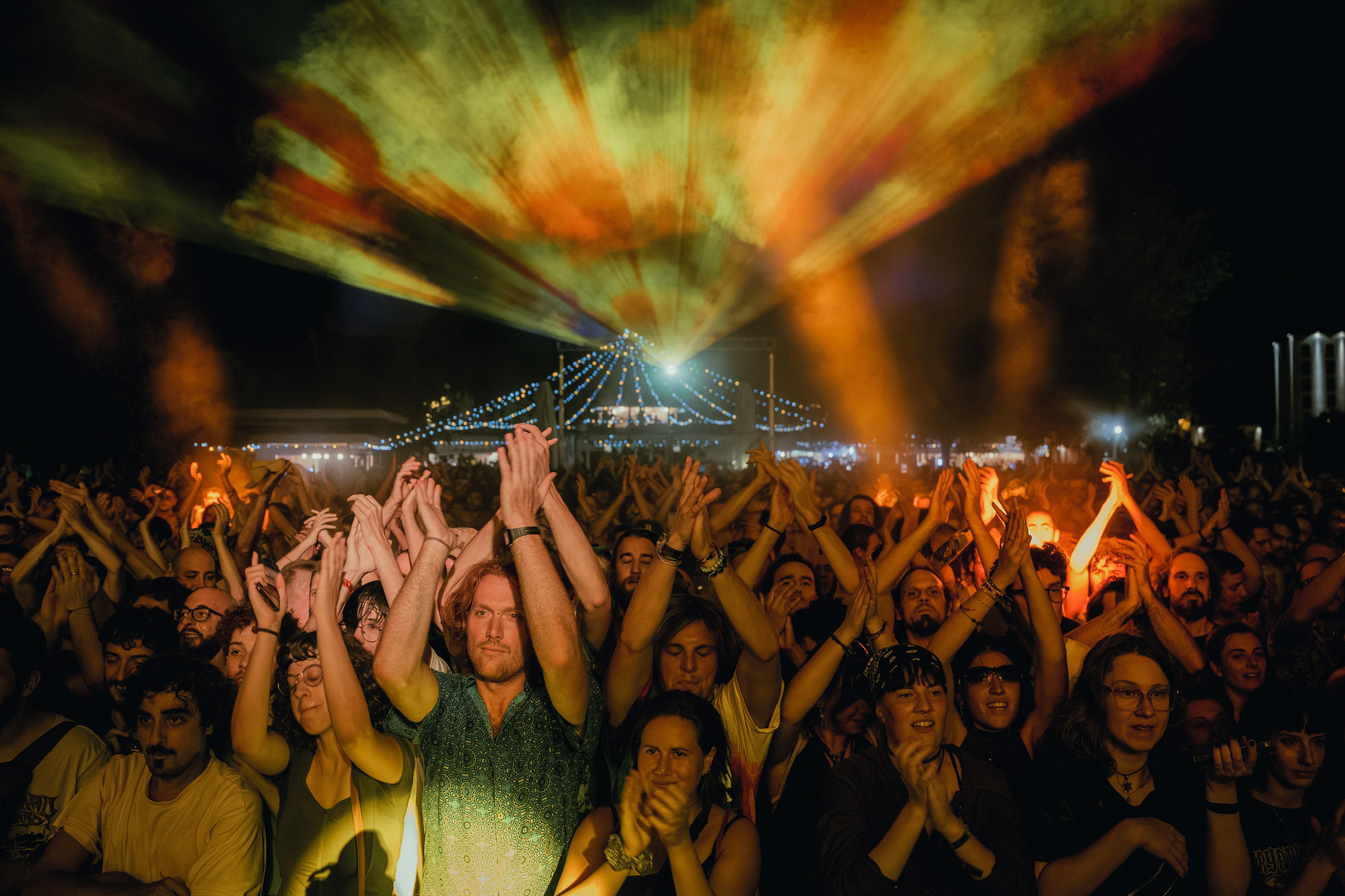 the energetic crowd bathed in stage light with lasers shooting overhead